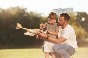 Fixing,, using screwdriver. Father and son are on the field together with toy plane. photo