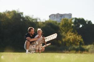 Playful mood. ..Father and son are on the field together with toy plane. photo