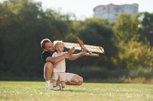 Screwdriver in hand, fixing it. Father and son are on the field together with toy plane, photo