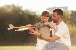 Fixing, using screwdriver. Father and son are on the field together with toy plane., photo
