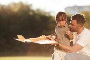 Broken, fixing it. Father and,, son, are ,on the field together with toy plane photo