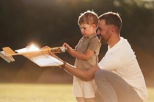 Illuminated by sunlight, fixing ,,,broken toy. Father and son are on the field together with plane photo