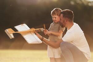 Illuminated, by sunlight, fixing broken toy. Father and son are on the field together with plane photo
