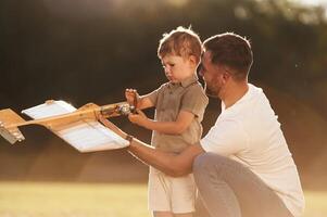 Illuminated ,,by, sunlight, fixing broken toy. Father and son are on the field together with plane photo