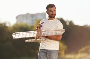 In casual clothes. Man is on ,the, field ,fixing the toy plane photo