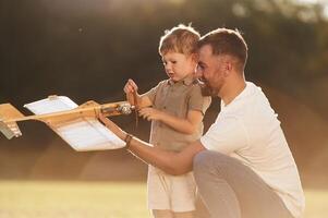 Illuminated by ,sunlight, fixing broken toy. Father and son are on the field together with plane photo
