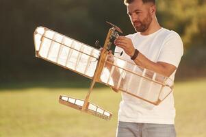 In casual clothes,. Man is on the field fixing the toy plane photo