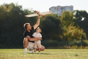 Having fun,, sitting., Father ,and ,son are on the field together with toy plane photo