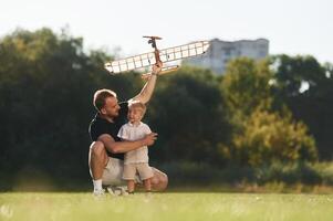 Having ,fun, sitting.,, Father and son are on the field together with toy plane photo