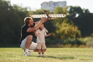 Having fun,, sitting,. Father, and son are on the field together with toy plane photo