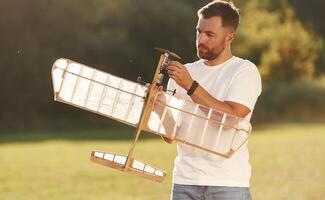 In, casual clothes. Man is on the field fixing the toy plane photo