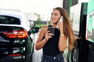 Having a conversation by phone. A young woman at a gas station with, her car photo