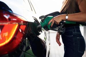 Pump nozzle, in the hand. A young woman at a gas station with her car photo