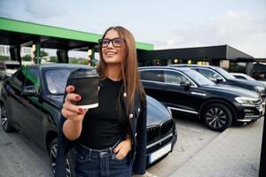 Happy owner with ,cup ,of, drink. A young woman at a gas station with her car photo