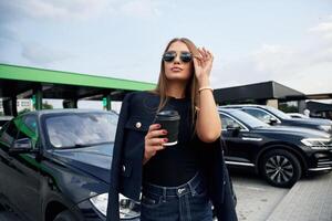 In sunglasses.. A young woman a,t a gas station with her car photo
