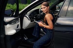 Looking, at, camera, holding smartphone. Woman is sitting in the car photo