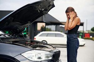 Hood is ,opened,,, shocked person. Woman's car is broken, accident, standing outdoors photo