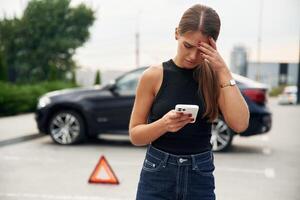 Trying, to catch the signal and help by phone. Woman's car is broken, accident, standing outdoors photo