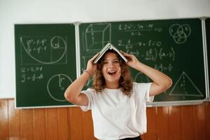 Fun, with notepad, over the head. Schoolgirl is standing against blackboard in the classroom photo