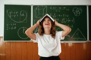 Fun,, with notepad over the head. Schoolgirl is standing against blackboard in the classroom photo