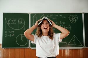Fun, with ,notepad over the head. Schoolgirl is standing against blackboard in the classroom photo
