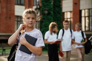 Portrait of girl, that is standing in front of her friends. Kids are near the school together, pupils photo