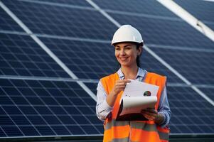 Notepad in hands. Female worker engineer in, uniform is near solar panels.. photo