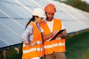 Reading the information from notepad.... Man and woman, workers are near solar panels, in uniform photo