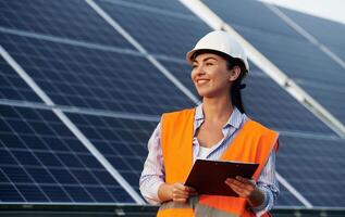 Notepad in hands. Female worker engineer in uniform is near solar panels. photo