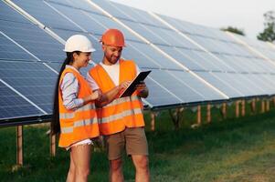 Reading the information from notepad. Man and woman, workers are near solar panels,. in uniform photo