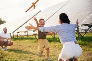 Running, to ,a ,,parent with toy plane. Father, mother and little son are outdoors near solar panels photo