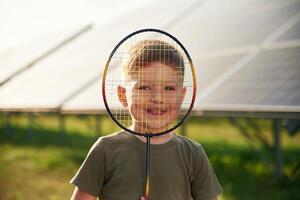 View ,through the badminton racket. Little boy is with solar panels outdoors photo