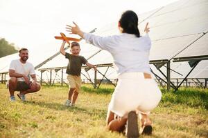 Running to a ,parent ,with toy plane. Father, mother and little son are outdoors near solar panels photo