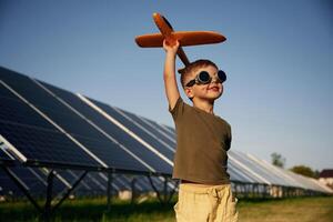 Time to, fly. Aviator glasses and toy ,plane. Little boy is with solar panels outdoors photo