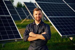 Portrait, standing,,,, with arms crossed. Man is working with solar panels outdoors at daytime photo