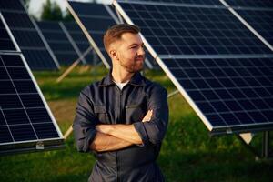 Portrait, standing with arms crossed,. Man is working with solar panels outdoors at daytime photo