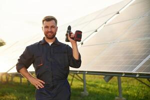 Ready, for, the work. With drill. Man is near solar panels outdoors at daytime photo