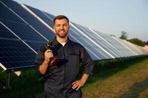 Outside, standing,, and holding the drill. Man is working with solar panels outdoors at daytime photo