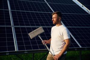 Mop in hands... Man is working with solar panels outdoors at daytime photo