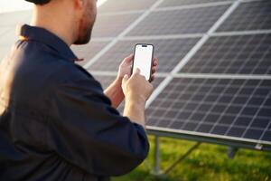 Phone in hands, ,internet connection. Man is working with solar panels outdoors at daytime photo