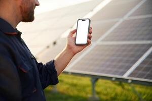 Smartphone with, copy space on it. Man is working with solar panels outdoors at daytime photo