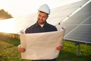 Paper plan, in hands. Man is working with solar panels outdoors at daytime photo
