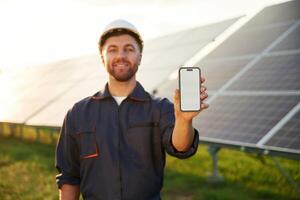 Smartphone with ,,copy space on it. Man is working with solar panels outdoors at daytime photo