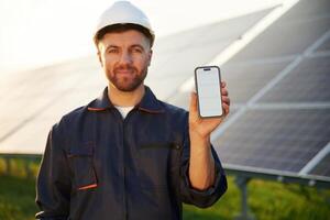 Smartphone with copy, space on it. Man is working with solar panels outdoors at daytime photo