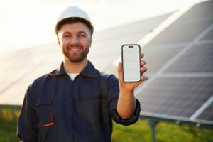 Smartphone, with copy space on it. Man is working with solar panels outdoors at daytime photo