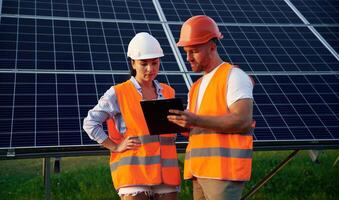 Reading, the ,information ,from notepad. Man and woman, workers are near solar panels, in uniform photo