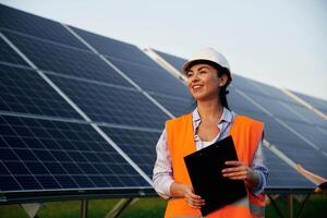 Black notepad ,in ,hands. Female worker engineer in uniform is near solar panels photo