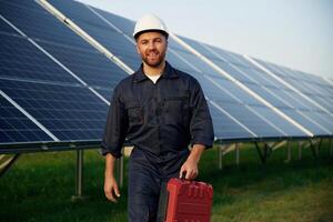 Red ,case, in hand. Man is working with solar panels outdoors at daytime photo
