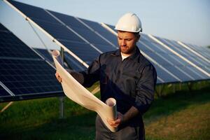 Paper ,,plan in hands. Man is working with solar panels outdoors at daytime photo