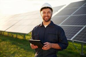 Digital ,tablet in,, hands. Man is working with solar panels outdoors at daytime photo